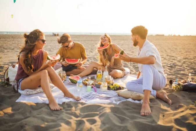 Un groupe d'amis partageant des tranches de pastèque fraîche lors d'un pique-nique de plage joyeux au coucher du soleil.