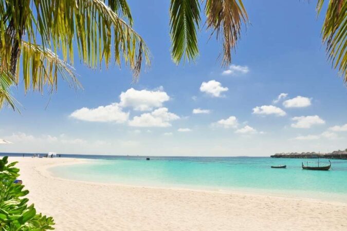 Une plage de sable fin et une eau turquoise bordées de palmiers dans un archipel tropical.