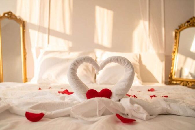 Des serviettes pliées en forme de cygnes avec des pétales de roses sur un lit dans un hôtel romantique.