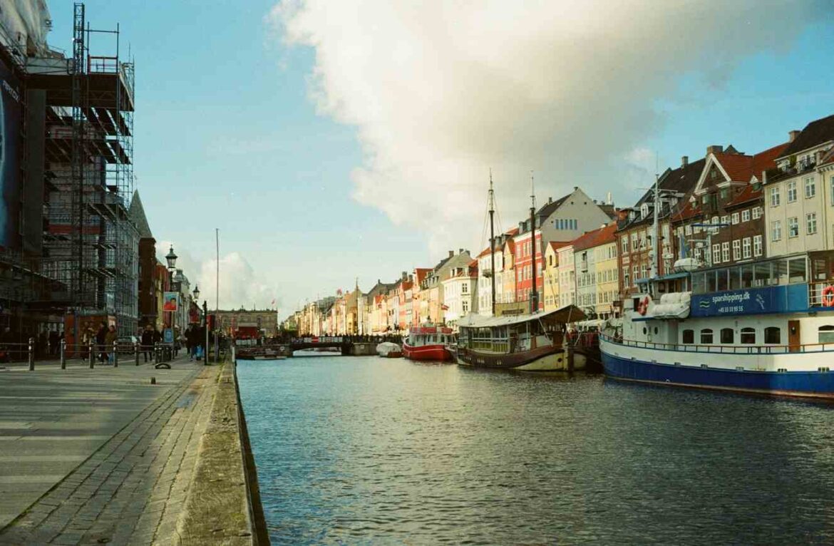 Les maisons colorées de Nyhavn à Copenhague au fil des saisons, avec des bateaux amarrés sur le canal sous un ciel lumineux.