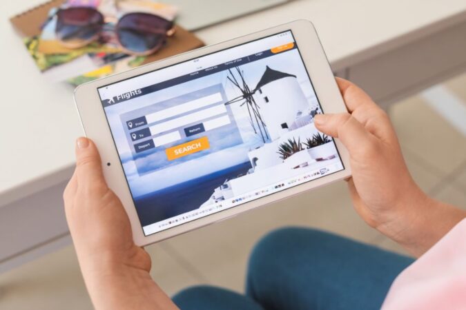 Une personne recherche un vol sur une tablette numérique pour organiser un voyage.